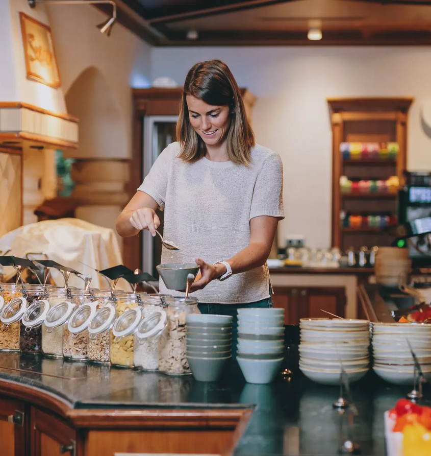 Frau schöpft Müsli am Frühstücksbuffet im Hotel Tyrol Haldensee
