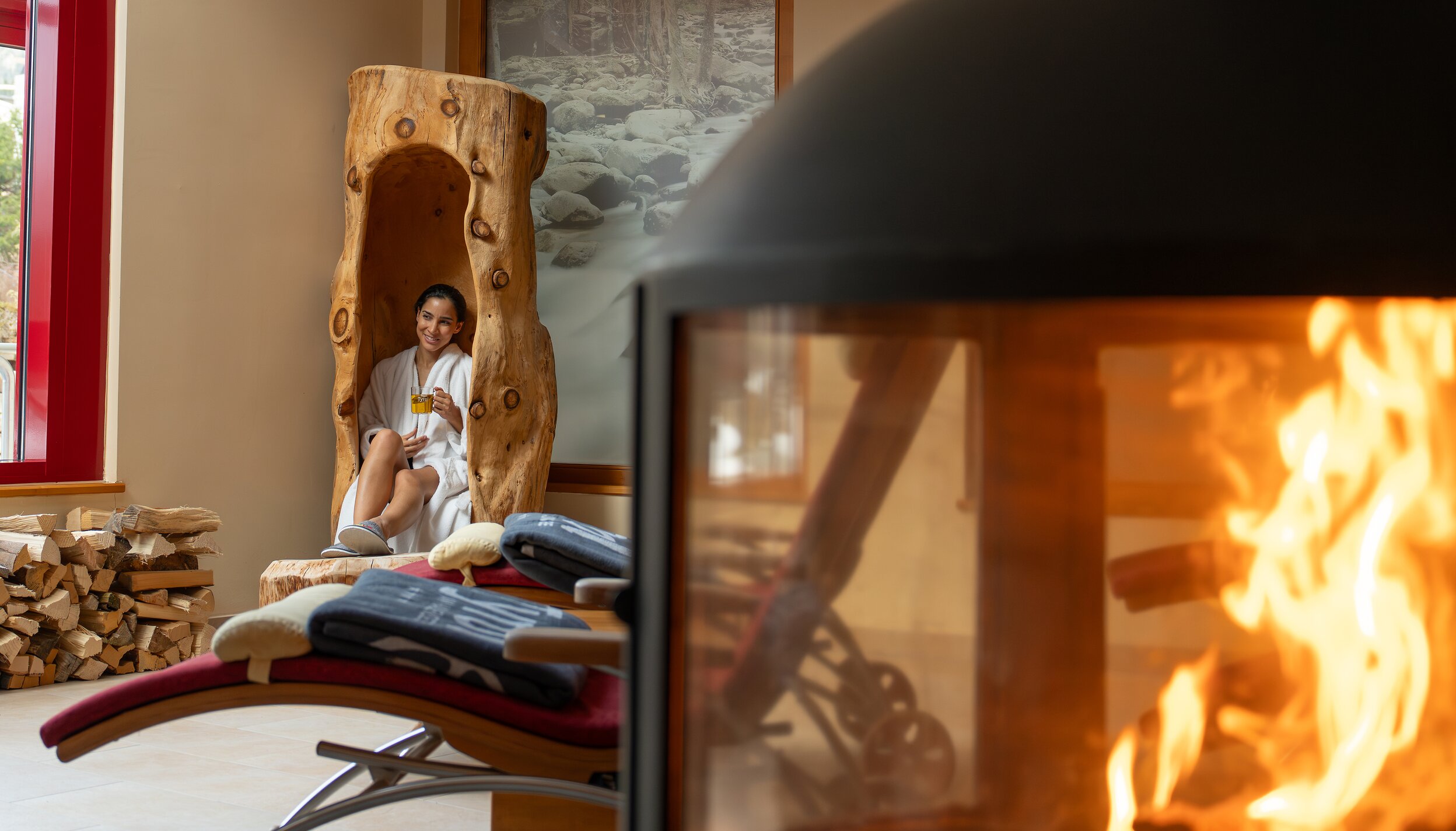 Frau im Bademantel in Baumstamm-Sitzgelegenheit neben Kamin